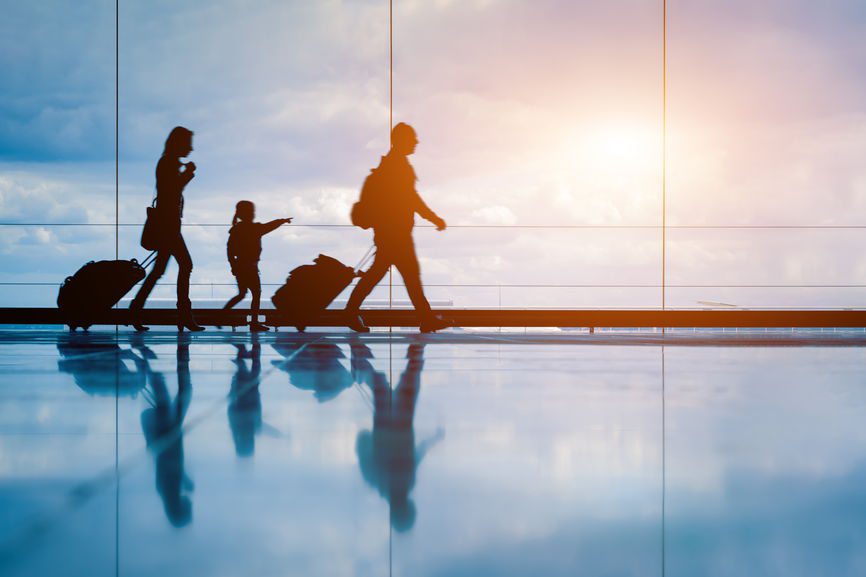 Family at airport travelling with young child and luggage walking to departure gate, girl pointing at airplanes through window, silhouette of people, abstract international air travel concept