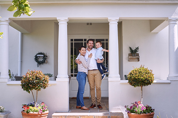 family stand proudly outside their first home in New Zealand